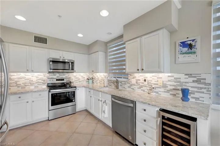 Kitchen with white cabinets, beverage cooler, appliances with stainless steel finishes, light tile patterned flooring, and light stone counters