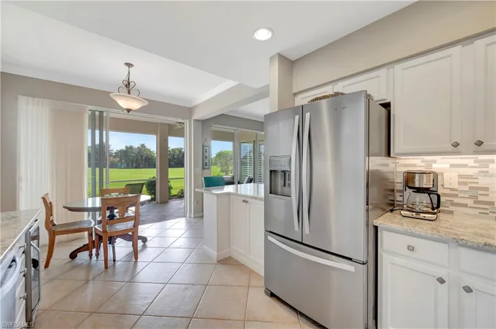 Kitchen with light stone countertops, hanging light fixtures, white cabinets, decorative backsplash, and stainless steel refrigerator with ice dispenser