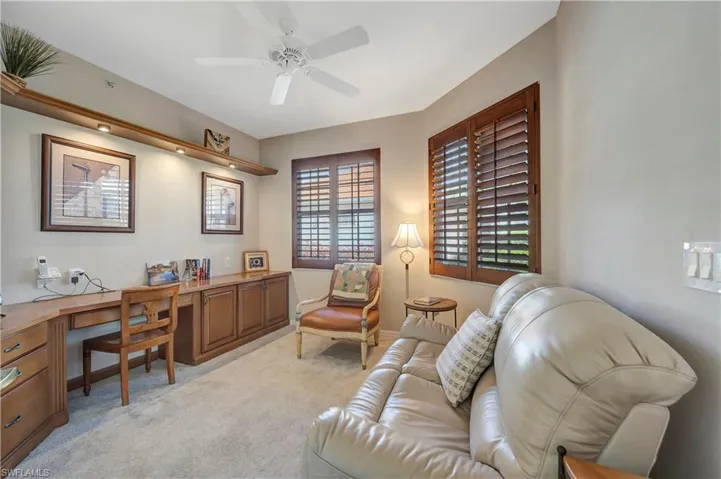 Carpeted office space with built in desk and wooden shutters.