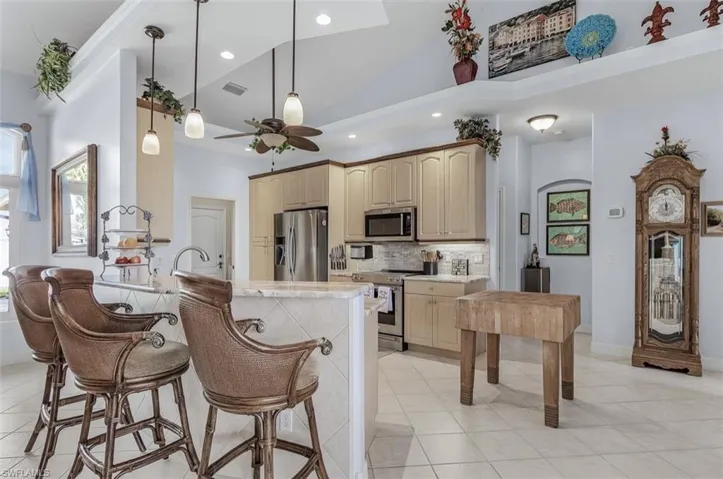 Kitchen with light tile patterned flooring, tasteful backsplash, appliances with stainless steel finishes, high vaulted ceiling, and ceiling fan