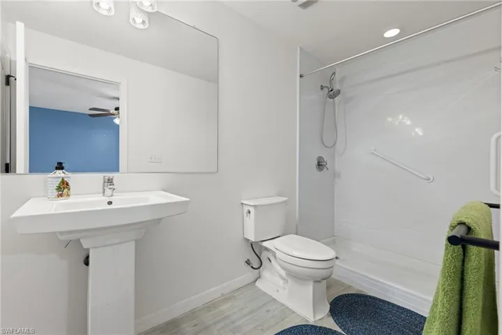 Bathroom featuring wood-type flooring, ceiling fan, toilet, and a shower