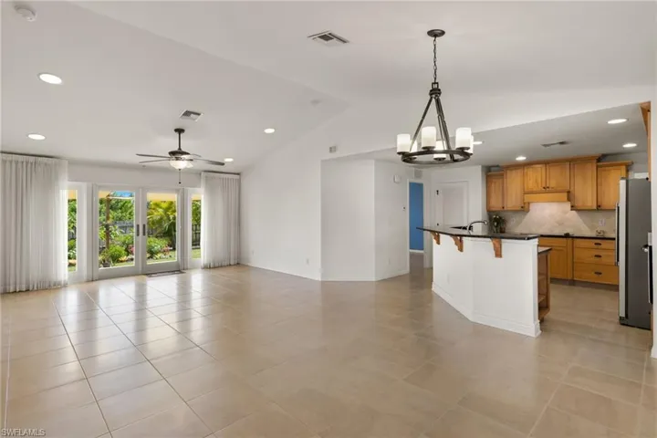 Kitchen featuring decorative light fixtures, ceiling fan with notable chandelier, backsplash, light tile floors, and stainless steel refrigerator