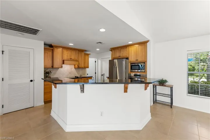 Kitchen featuring a center island, stainless steel appliances, backsplash, a breakfast bar, and light tile floors