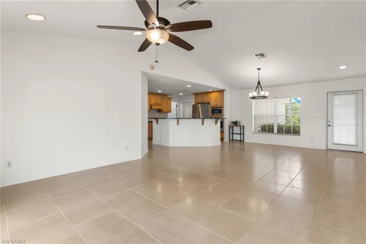 Unfurnished living room with vaulted ceiling, light tile floors, and ceiling fan with notable chandelier