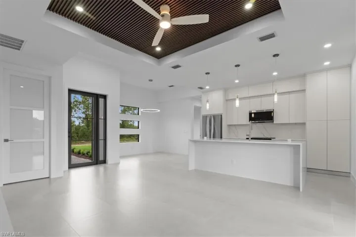 Kitchen with modern cabinets, a raised ceiling, an island with sink, white cabinets, and stainless steel appliances