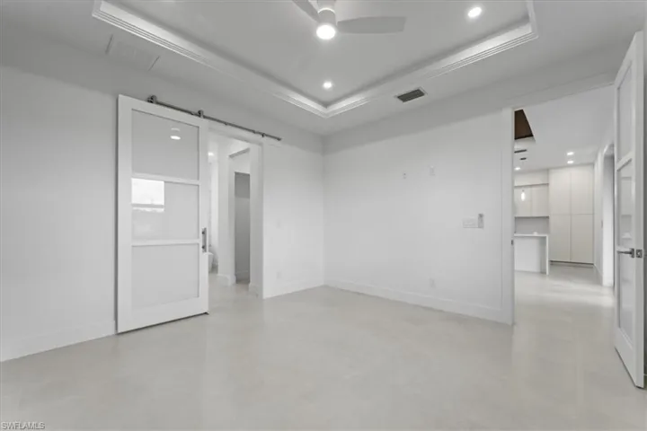 Empty room with a barn door, recessed lighting, a tray ceiling, ceiling fan, and concrete flooring