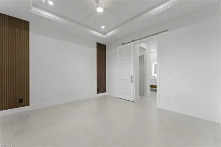 Spare room featuring a barn door, a tray ceiling, ceiling fan, recessed lighting, and finished concrete floors
