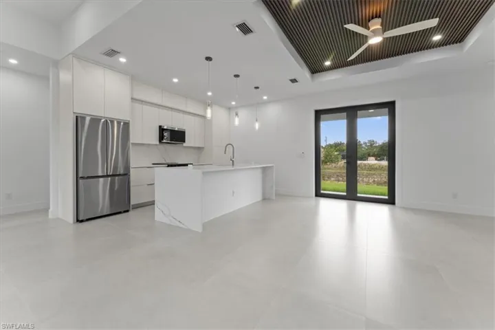 Kitchen featuring stainless steel appliances, a kitchen island with sink, decorative light fixtures, open floor plan, and white cabinetry