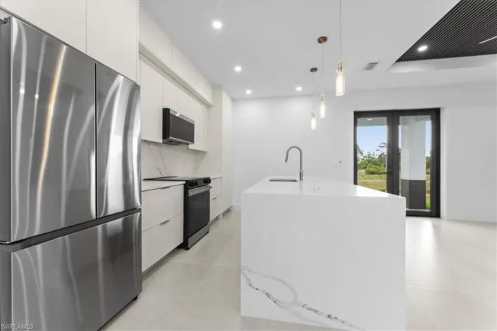 Kitchen featuring stainless steel appliances, modern cabinets, hanging light fixtures, white cabinets, and light stone counters