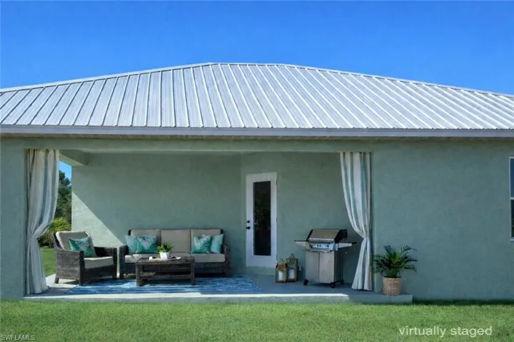 Rear view of house with stucco siding, a patio area, a metal roof, an outdoor lounge area, and a lawn