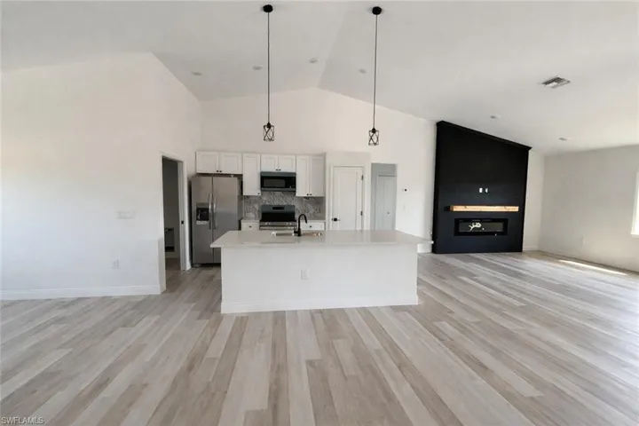 Kitchen with open floor plan, white cabinets, black appliances, decorative light fixtures, and a kitchen island with sink