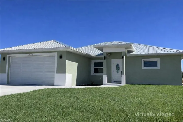 View of front facade with an attached garage, stucco siding, a front lawn, concrete driveway, and a metal roof