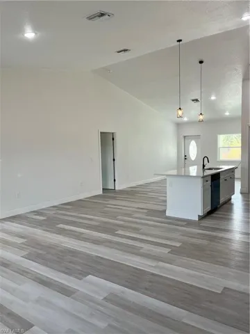 Kitchen featuring open floor plan, decorative light fixtures, a center island with sink, light wood finished floors, and lofted ceiling