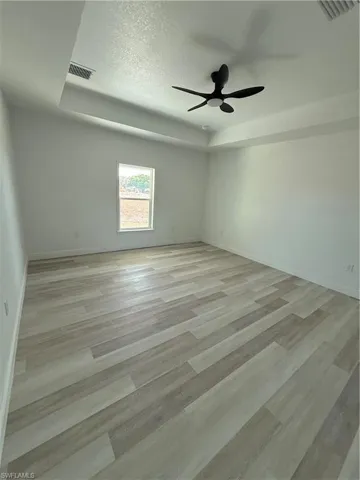 Spare room featuring a tray ceiling, a textured ceiling, light wood-style floors, and a ceiling fan