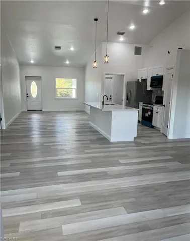 Kitchen featuring open floor plan, white cabinets, electric range, hanging light fixtures, and a center island with sink