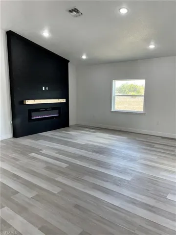 Unfurnished living room featuring a glass covered fireplace, recessed lighting, light wood finished floors, and a textured ceiling