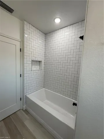 Full bath with light wood-type flooring, shower / washtub combination, and a textured ceiling