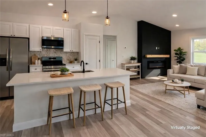 Kitchen with stainless steel appliances, a breakfast bar area, an island with sink, white cabinetry, and a large fireplace
