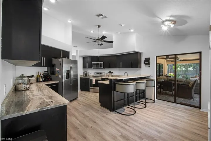 Kitchen with appliances with stainless steel finishes, light hardwood / wood-style flooring, ceiling fan, and high vaulted ceiling
