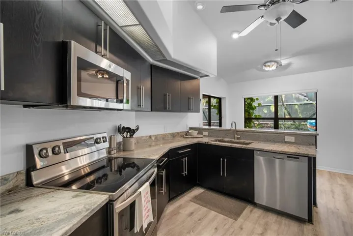 Kitchen featuring stainless steel appliances, light hardwood / wood-style floors, light stone counters, and sink