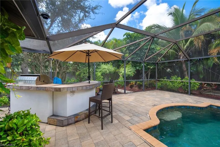View of swimming pool featuring a lanai, exterior kitchen, area for grilling, an outdoor bar, and a patio area