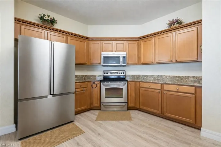 Kitchen featuring stainless steel appliances, dark stone counters, wood finish cabinetry, and light wood-style flooring