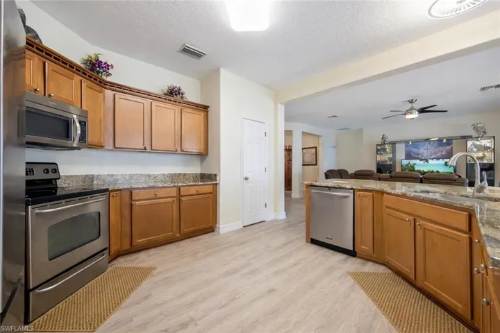 Kitchen featuring stainless steel appliances, open floor plan, wood finish cabinets, light stone countertops, and a textured ceiling