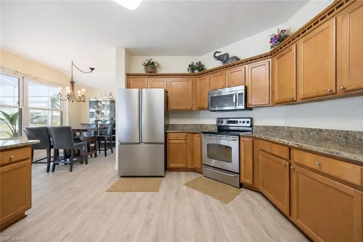 Kitchen featuring stainless steel appliances, dark stone countertops, wood finish cabinets, light wood finished floors, and hanging lights