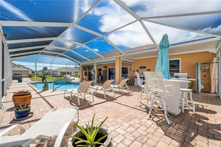 Outdoor pool with a sunroom, a patio area, glass enclosure, and exterior bar