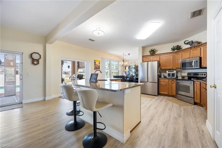 Kitchen featuring a kitchen bar, stainless steel appliances, wood finish cabinets, an island with sink, and light wood-style floors