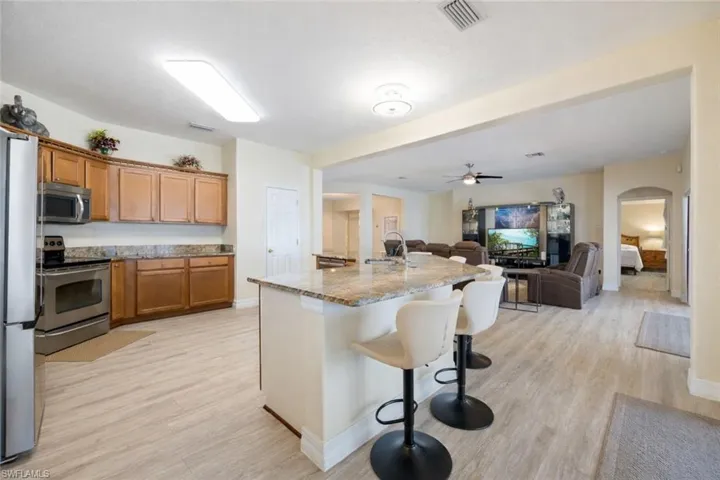 Kitchen with wood finish cabinetry, stainless steel appliances, light wood-style floors, open floor plan, and a kitchen bar