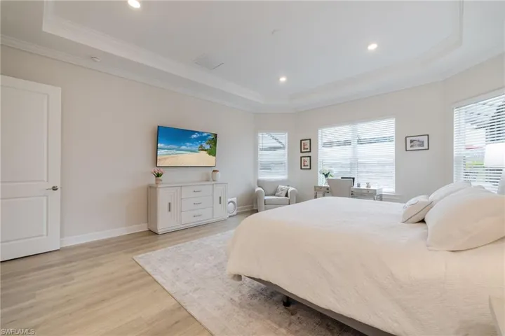 Bedroom featuring light wood-style floors, a raised ceiling, recessed lighting, and crown molding
