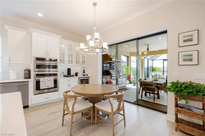 Dining space with a chandelier, light wood-style floors, ceiling fan, crown molding, and beverage cooler