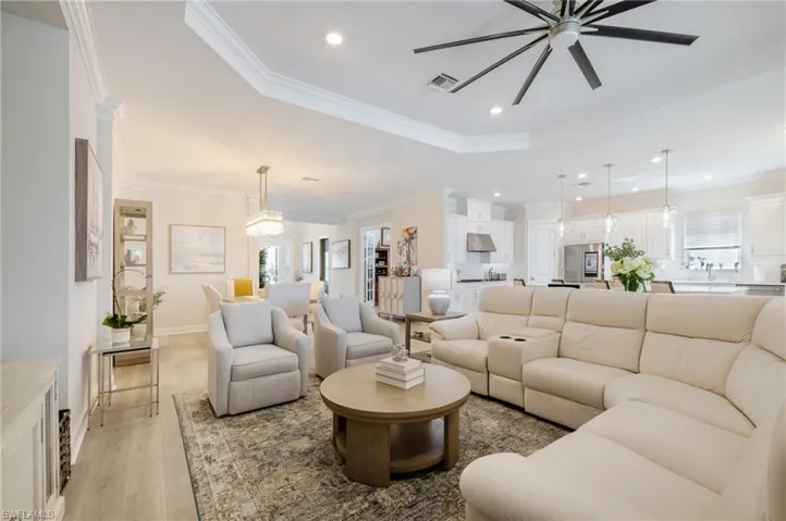 Living area featuring a ceiling fan, light wood-style floors, recessed lighting, crown molding, and a tray ceiling