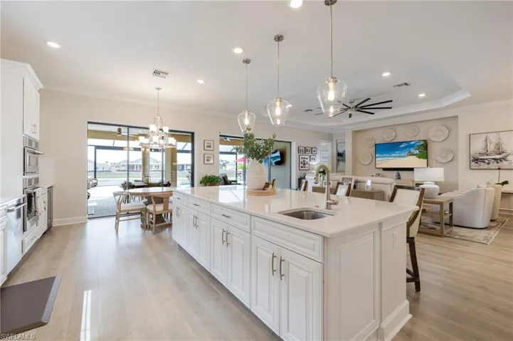 Kitchen featuring white cabinetry, a breakfast bar, light stone counters, crown molding, and a kitchen island with sink