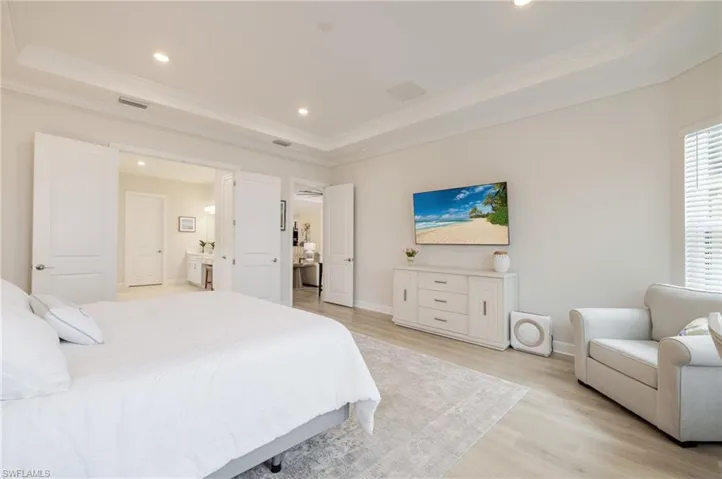 Bedroom with light wood-style floors, ornamental molding, recessed lighting, a tray ceiling, and connected bathroom