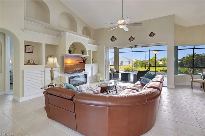 Tiled living room with built in features, ceiling fan, and high vaulted ceiling