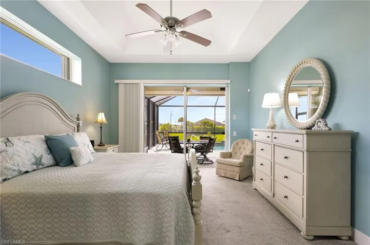 Master bedroom featuring access to pool deck, ceiling fan, and a raised ceiling