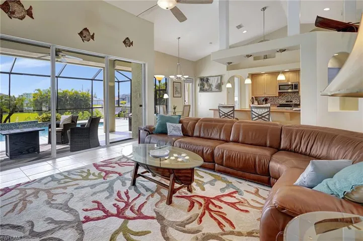 Living room with high vaulted ceiling, beamed ceiling, ceiling fan with notable chandelier, and light tile patterned floors