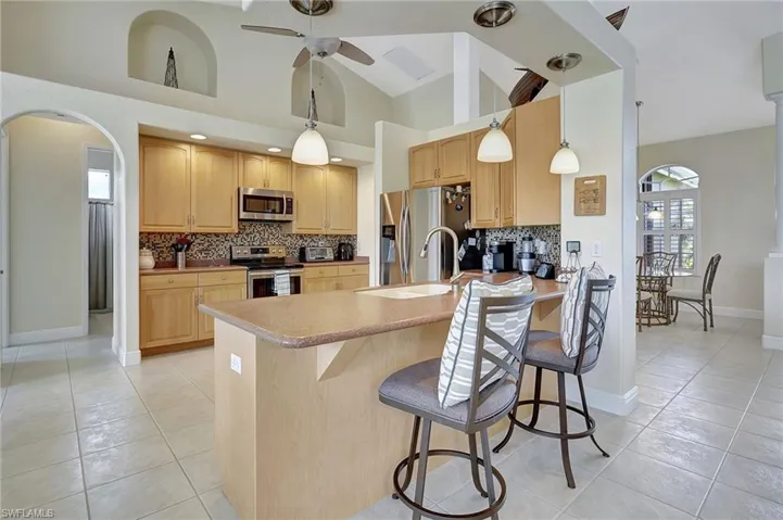 Kitchen featuring appliances with stainless steel finishes, a breakfast bar area, tasteful backsplash, decorative light fixtures, and high vaulted ceiling