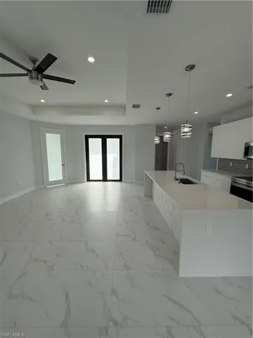 Kitchen with a large island, pendant lighting, sink, white cabinetry, and backsplash