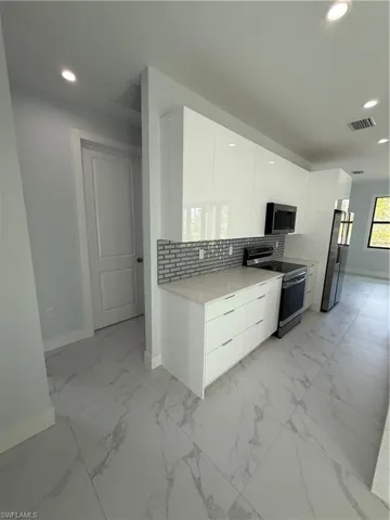 Kitchen featuring white cabinets, refrigerator, decorative backsplash, and stove
