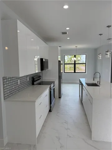 Kitchen with stove, sink, decorative light fixtures, and white cabinets
