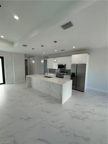 Kitchen with sink, refrigerator, stove, hanging light fixtures, and white cabinetry