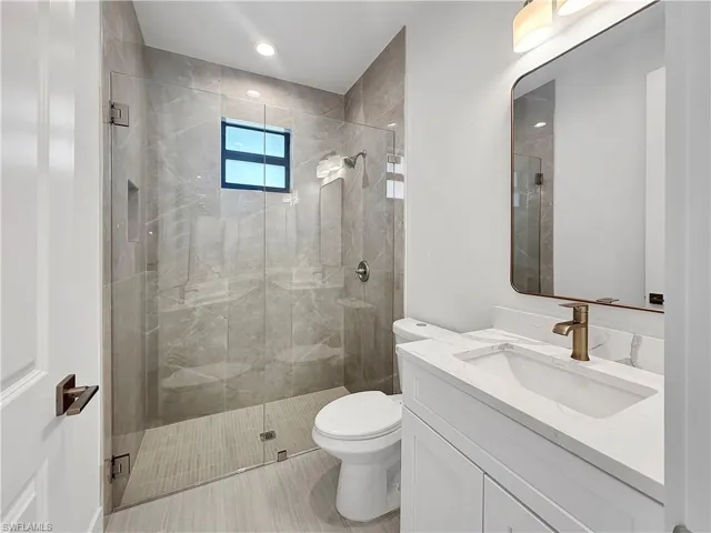 Bathroom with toilet, a tile shower, and vanity