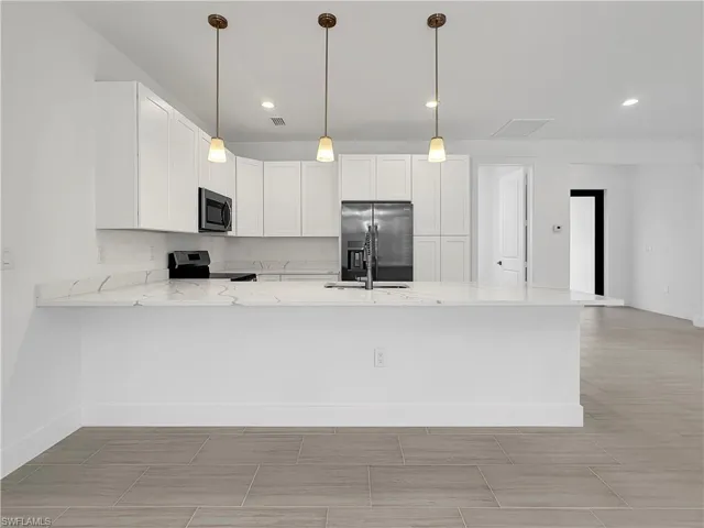 Kitchen with white cabinetry, appliances with stainless steel finishes, light stone counters, light tile patterned floors, and kitchen peninsula