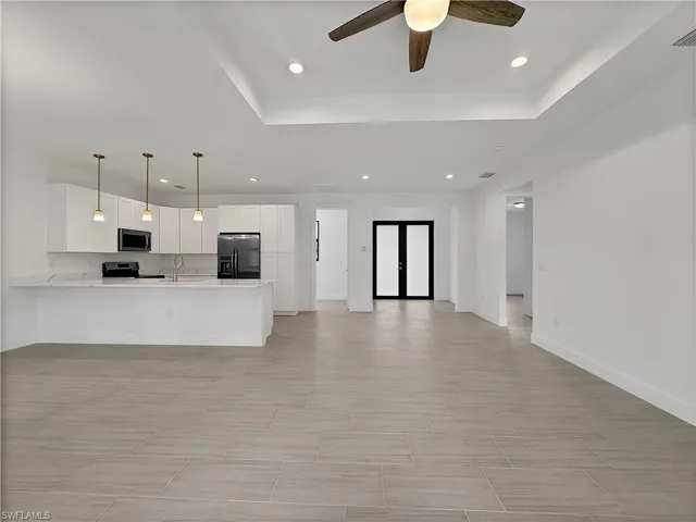 Unfurnished living room with light tile patterned floors, a raised ceiling, sink, and ceiling fan