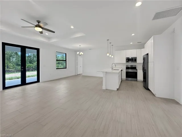 Kitchen with stainless steel appliances, a center island with sink, ceiling fan with notable chandelier, a tray ceiling, and hanging light fixtures