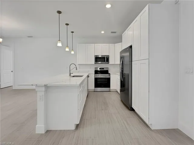 Kitchen with hanging light fixtures, appliances with stainless steel finishes, light stone countertops, sink, and kitchen peninsula