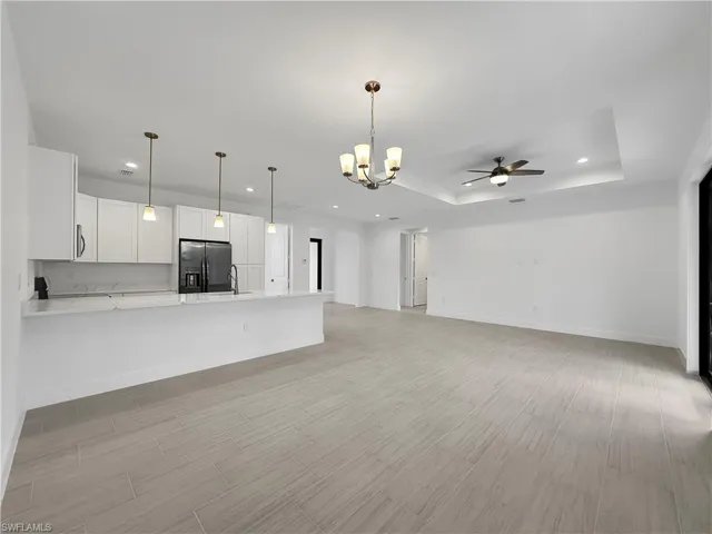 Unfurnished living room featuring ceiling fan with notable chandelier and a raised ceiling